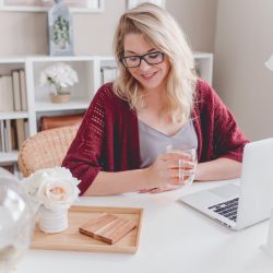 woman smiling holding glass mug sitting beside table with MacBook